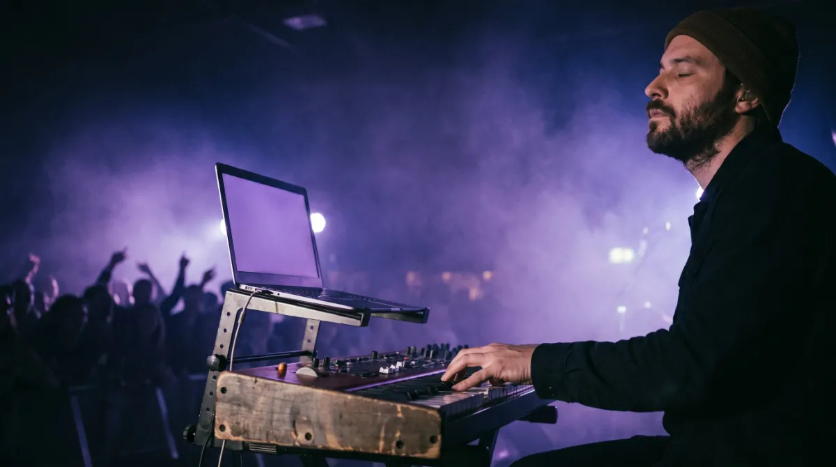 A worship keyboardist on a dark stage between songs, purple haze and a congregation far behind